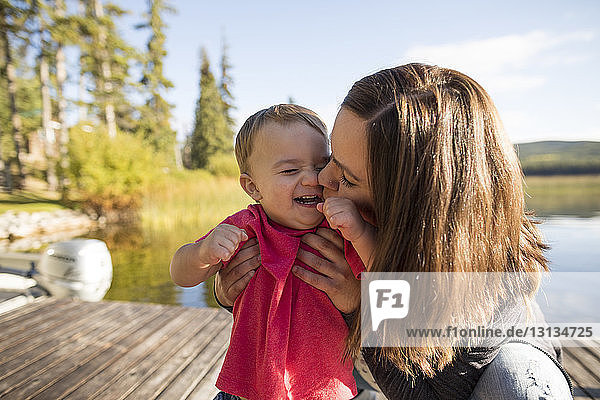 Mother kissing cheerful son on pier against lake