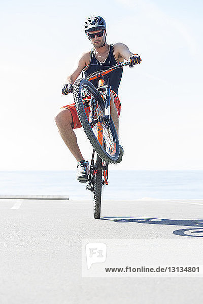 Mann führt Stunt mit Fahrrad gegen das Meer an einem sonnigen Tag aus