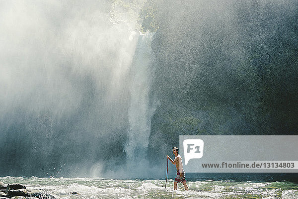 Mann geht in flachem Wasser gegen Wasserfall
