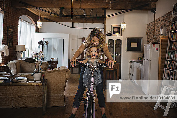 Glückliche Mutter mit Tochter fährt zu Hause Fahrrad