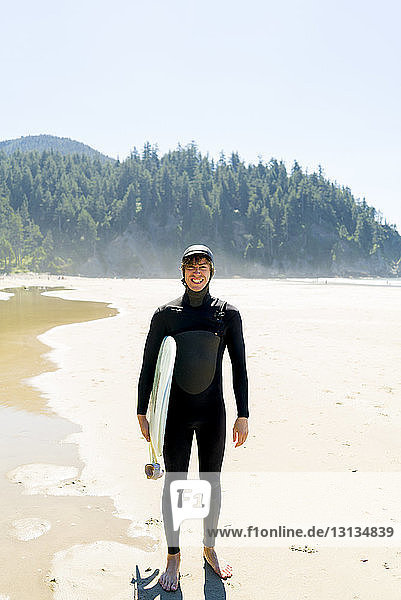 Porträt eines glücklichen Mannes  der ein Surfbrett hält  während er am Strand steht