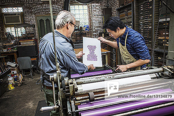 Workers examining paper by letterpress at workshop