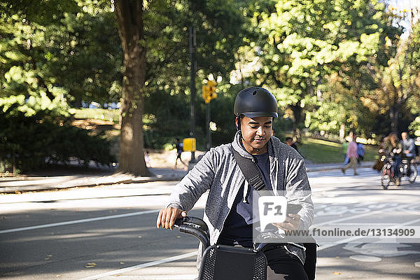 Mann benutzt Mobiltelefon beim Fahrradfahren auf der Straße in der Stadt