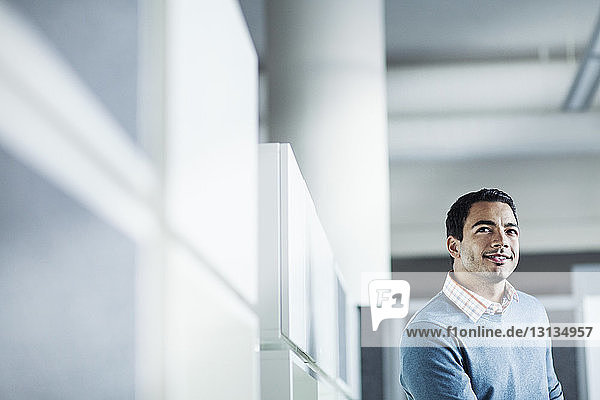 Smiling businessman standing by wall in office