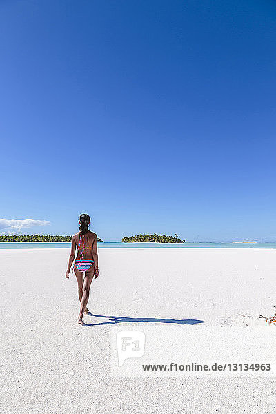 Rear view of woman walking on sand at beach against blue sky during sunny day