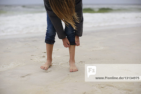 Mädchen rollt am Strand Jeans auf