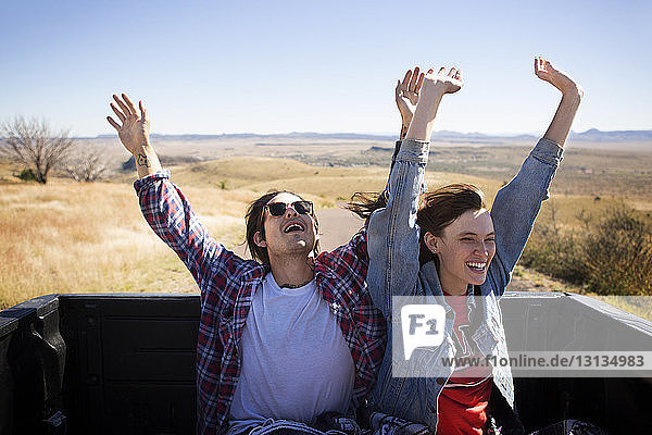 Happy couple with arms raised traveling in pick-up truck