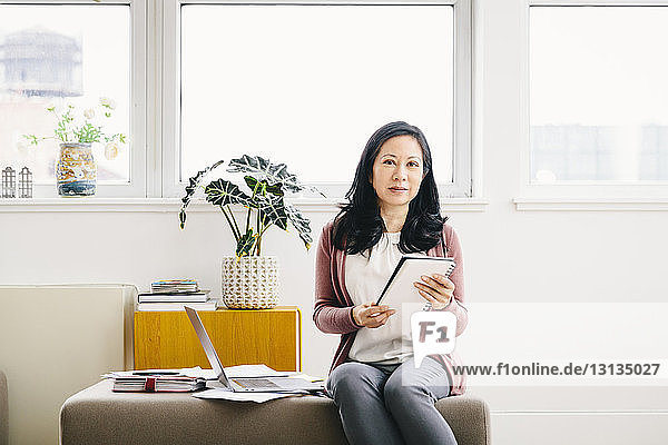 Porträt einer selbstbewussten Geschäftsfrau  die ein Spiral-Notizbuch hält  während sie im Büro sitzt