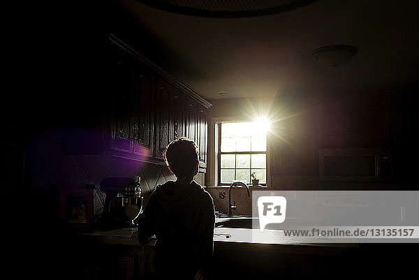 Scherenschnitt-Junge  der in der Küche stehend durch das Fenster in die Sonne schaut