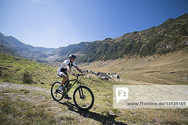 Man riding bicycle on grass field against mountains