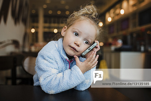 Nahaufnahme eines Mädchens  das ein Mobiltelefon benutzt  während es am Tisch im Restaurant sitzt