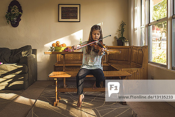 Mädchen spielt Geige  während sie zu Hause auf einem Holzsitz sitzt