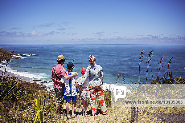 Rear view of family standing on hill and looking at sea against sky