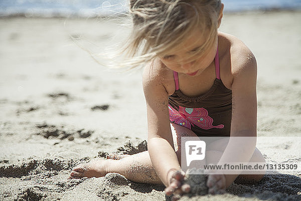 Mädchen spielt mit Sand am Strand an einem sonnigen Tag