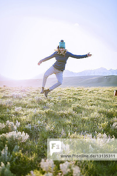 Wanderin springt in voller Länge auf Grasfeld gegen den Himmel