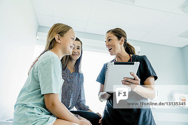 Low angle view of surprised pediatrician holding tablet computer while looking at girl sitting by mother in medical examination room