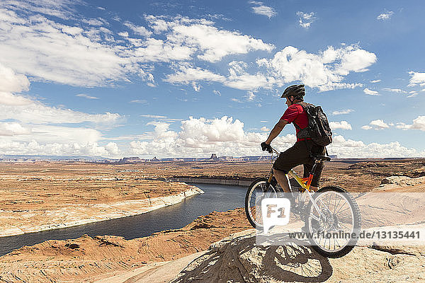 Mountain biker with bicycle standing on rock formation against cloudy sky