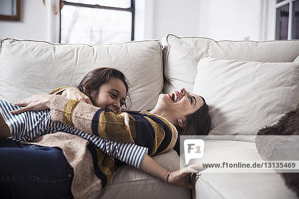 Fröhliche Mutter und Tochter genießen zu Hause auf dem Sofa