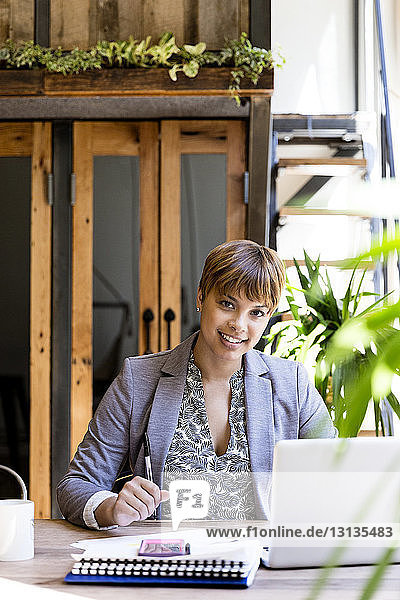 Porträt einer lächelnden  mittleren erwachsenen Geschäftsfrau  die am Schreibtisch einen Laptop benutzt