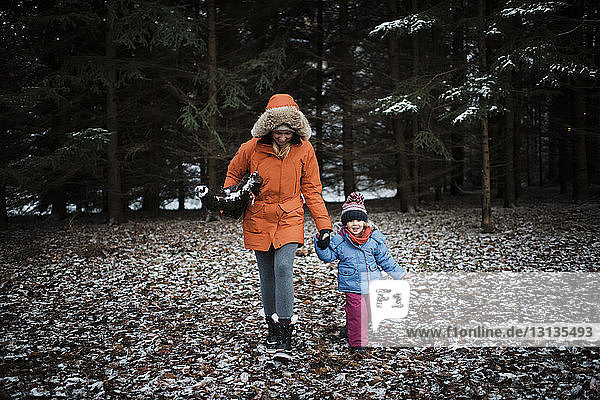 Mother and daughter in warm clothing walking at forest during winter