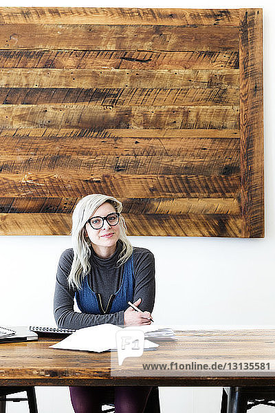 Porträt einer jungen Geschäftsfrau  die im Büro an einem Holztisch sitzt
