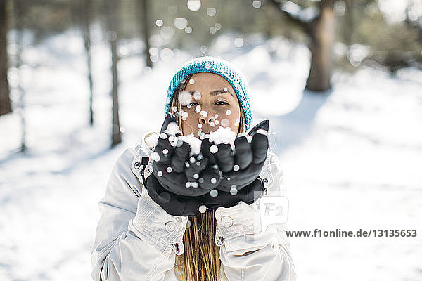 Frontansicht einer Frau  die Schnee bläst  während sie auf dem Feld steht