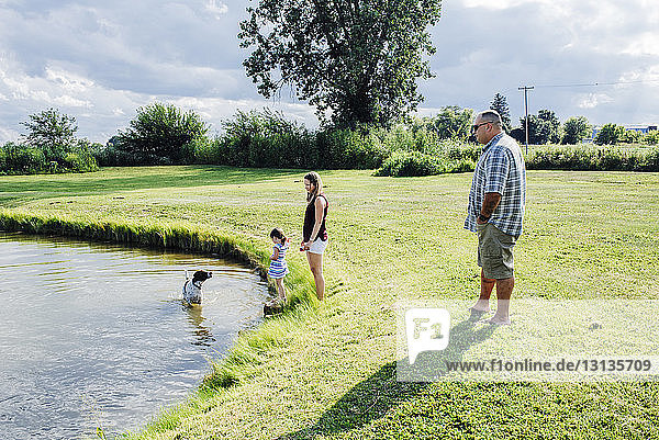 Familie betrachtet Hund im See stehend vor bewölktem Himmel