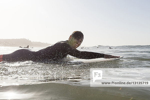 Porträt eines glücklichen männlichen Surfers in Seitenansicht  der bei Sonnenuntergang auf einem Surfbrett im Meer liegt