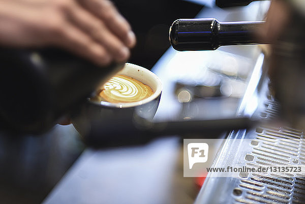 Abgehackte Hand eines Barista gießt Milch in Kaffee  während er im Café ein schaumiges Getränk zubereitet