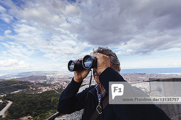 Man using binoculars while standing against cloudy sky
