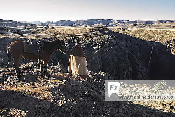 Rückansicht einer Frau  die zu Pferd auf einem Berg vor klarem Himmel steht