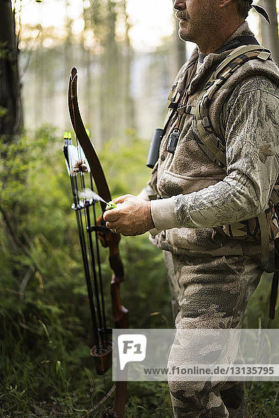Midsection of hunter holding bow and arrow while standing in forest