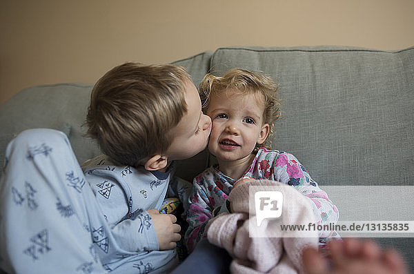 Boy kissing sister while sitting on sofa at home
