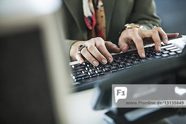 Beschnittenes Bild einer Frau  die auf der Computertastatur am Büroschreibtisch tippt
