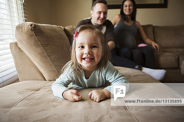 Porträt eines niedlichen Mädchens  das liegt  während die Eltern zu Hause auf dem Sofa sitzen