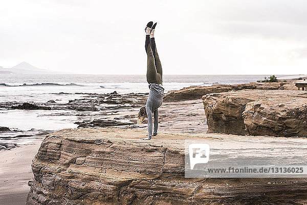 Full length of woman practicing handstand on rock at beach