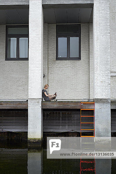Seitenansicht einer Geschäftsfrau  die einen Tablet-Computer benutzt  während sie im Korridor am Kanal sitzt