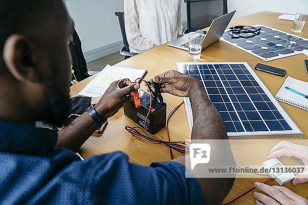 Nahaufnahme eines Geschäftsmannes  der Metallklammern an der Batterie anbringt  während er an einem Solarpanel-Modell arbeitet