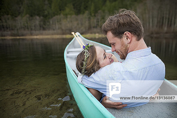 Young couple looking each other face to face while relaxing in canoe on lake