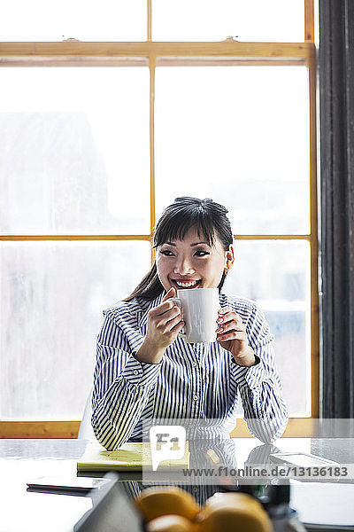 Lächelnde Geschäftsfrau  die Kaffee trinkt  während sie im Büro am Tisch sitzt