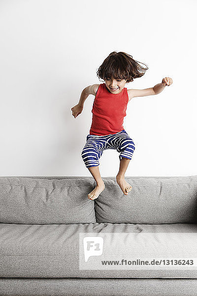 Happy boy jumping on sofa against wall at home