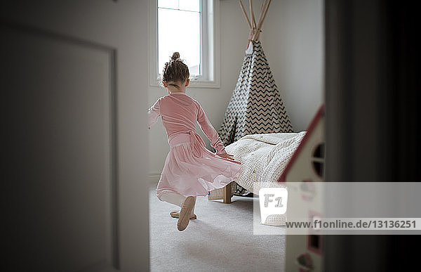 Rear view of girl in ballet costume dancing at home seen through doorway