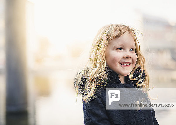 Lächelndes Mädchen schaut weg  während es draußen einen Mantel trägt