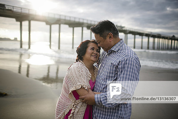 Frau umarmt Mann  während sie am Strand auf Sand steht