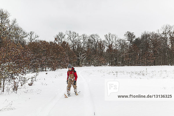 Teenage boy wearing snowshoes walking on snow covered field in forest against sky