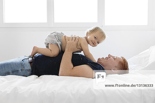Side view of happy father with shirtless daughter lying on bed at home