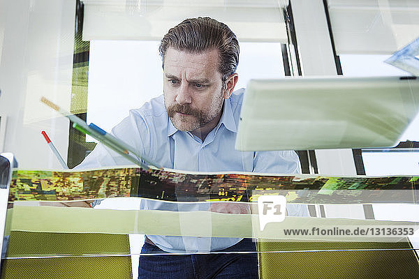 Niederwinkelansicht eines kreativen Geschäftsmannes beim Analysieren von Fotos am gläsernen Konferenztisch