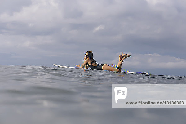Seitenansicht einer Frau beim Surfen auf dem Meer vor bewölktem Himmel