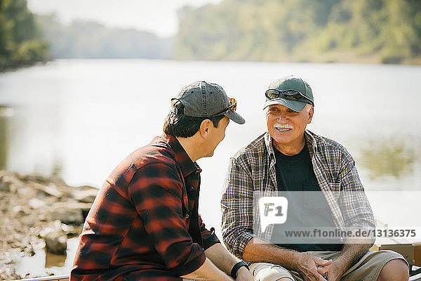 Male friends talking while sitting on boat at lakeshore