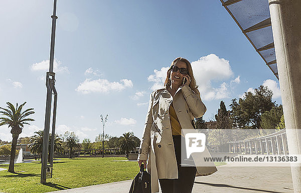 Niedriger Blickwinkel einer Geschäftsfrau  die mit ihrem Handy telefoniert  während sie im Park gegen den Himmel läuft